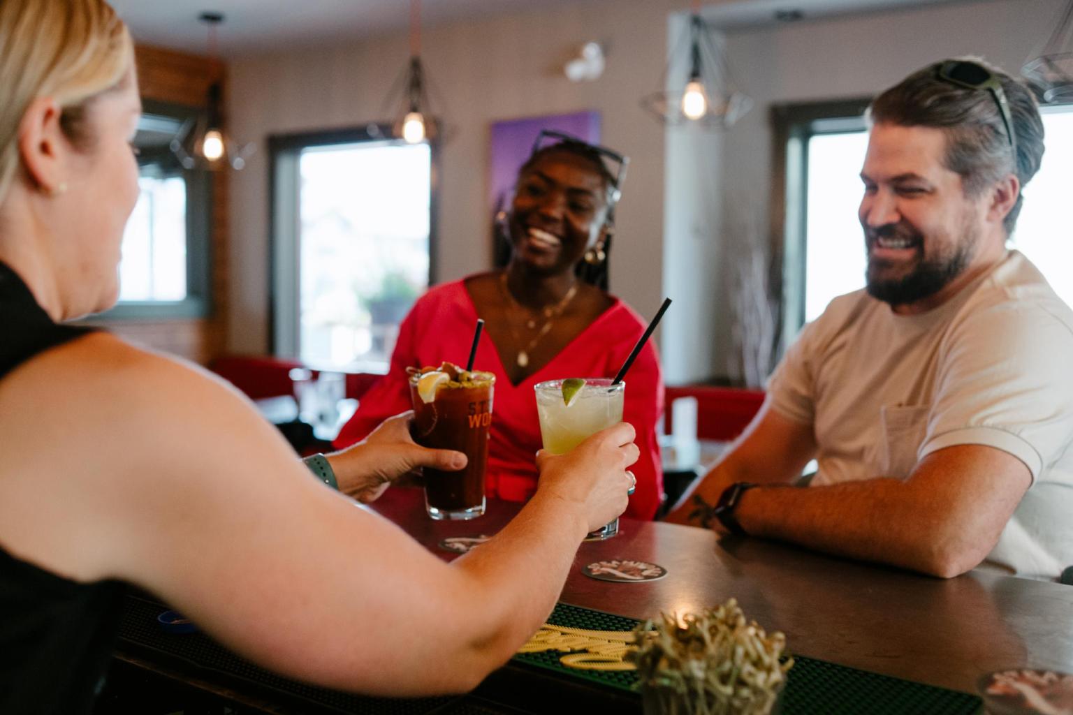 Three people smiling and clinking drinks at a bar.