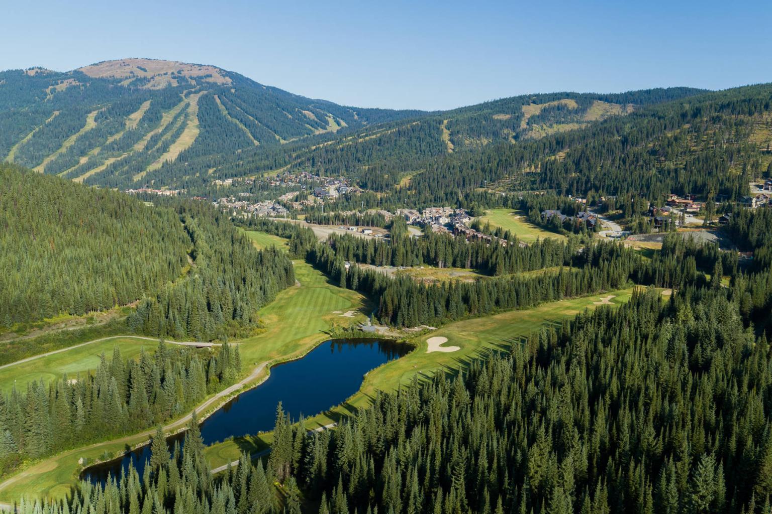 Mountain landscape with lush greenery, a small lake, and distant village.