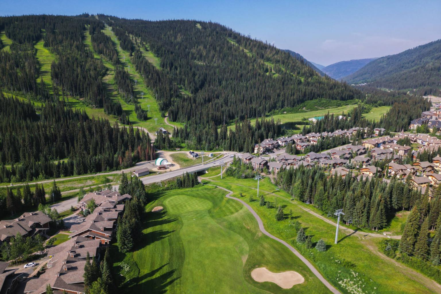 Aerial view of a golf course surrounded by mountains and a residential area.