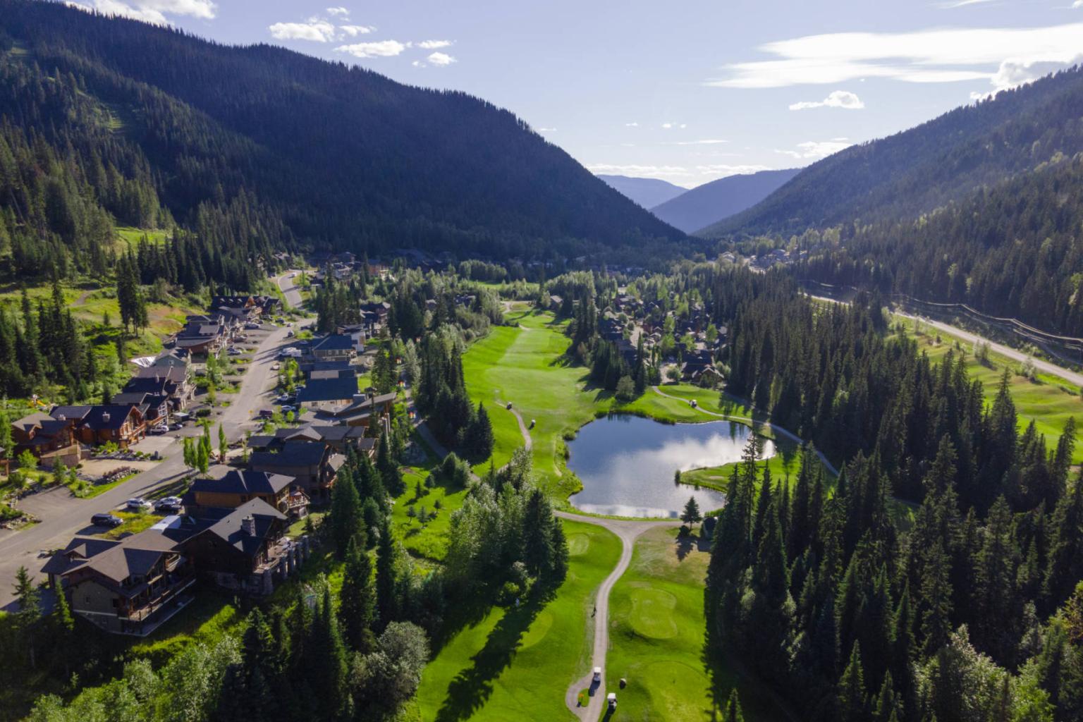 Mountain valley with a lake, road, and houses under a clear blue sky.
