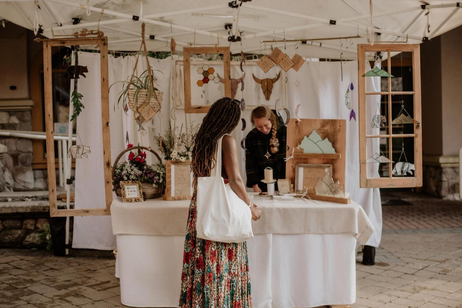 Market stall with crafts and greenery; woman browsing under a canopy.