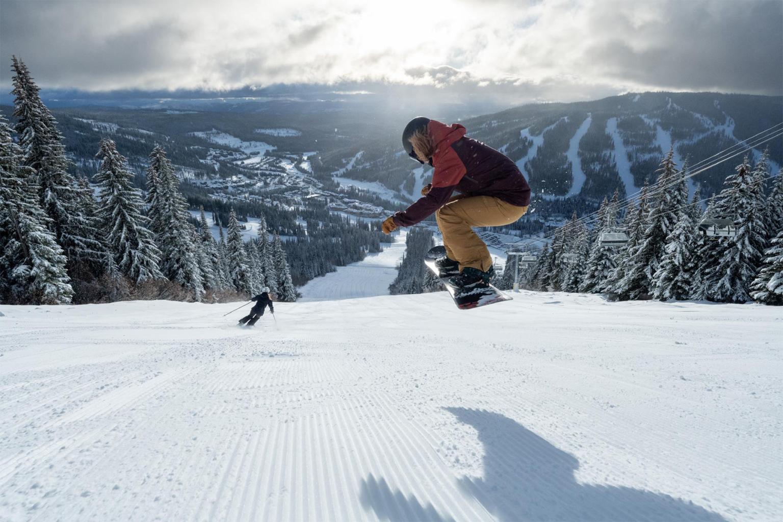 Snowboarder jumping on a snowy mountain slope with trees in the background.