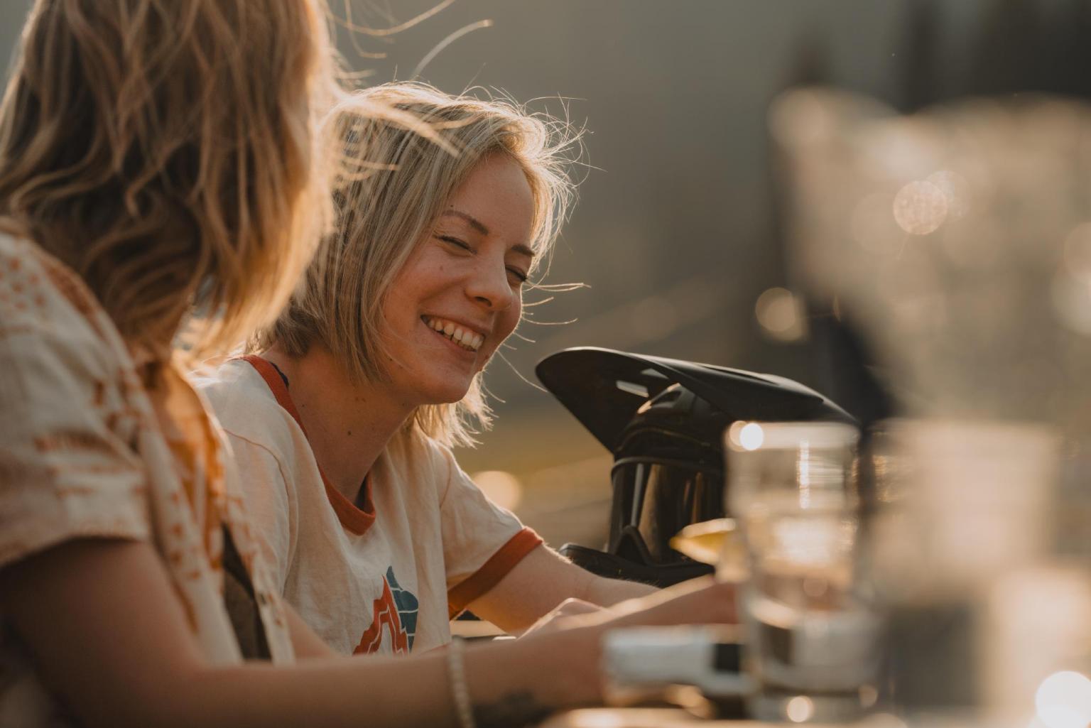 Two people smiling and talking outdoors in warm sunlight.