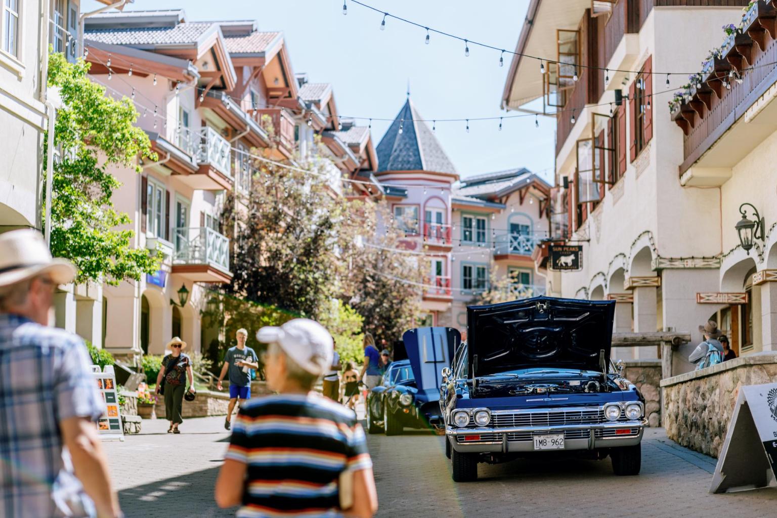 A classic car with an open hood on a pedestrian street, people walking nearby.