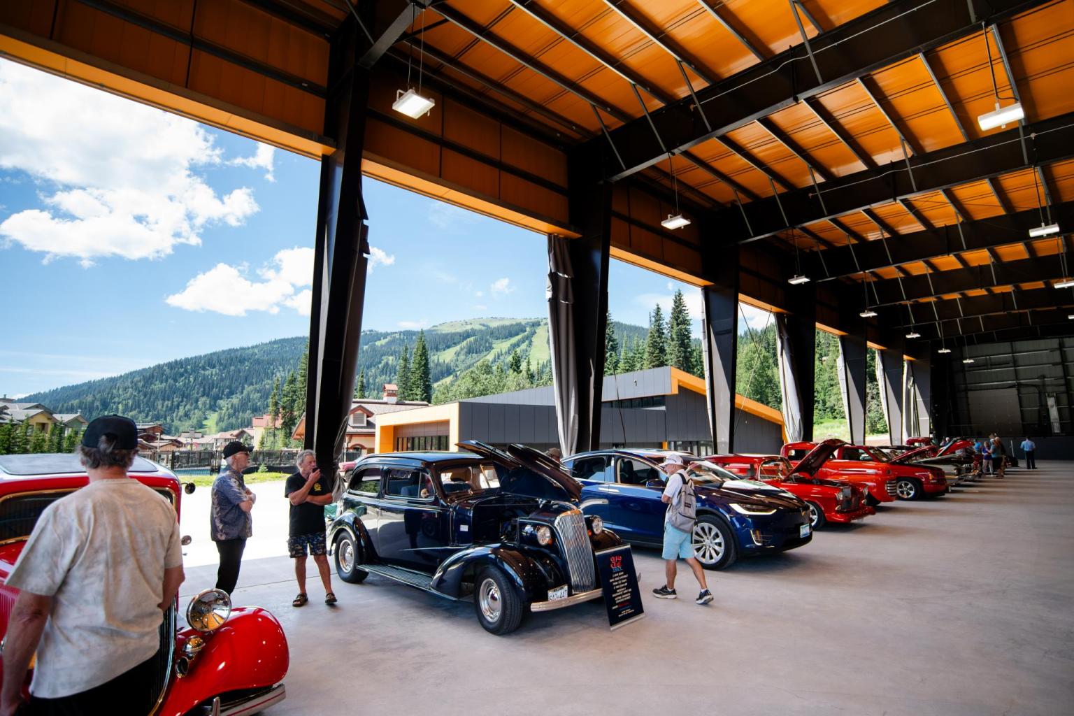 Classic cars displayed in the Sun Peaks Centre arena, with mountains in the background.