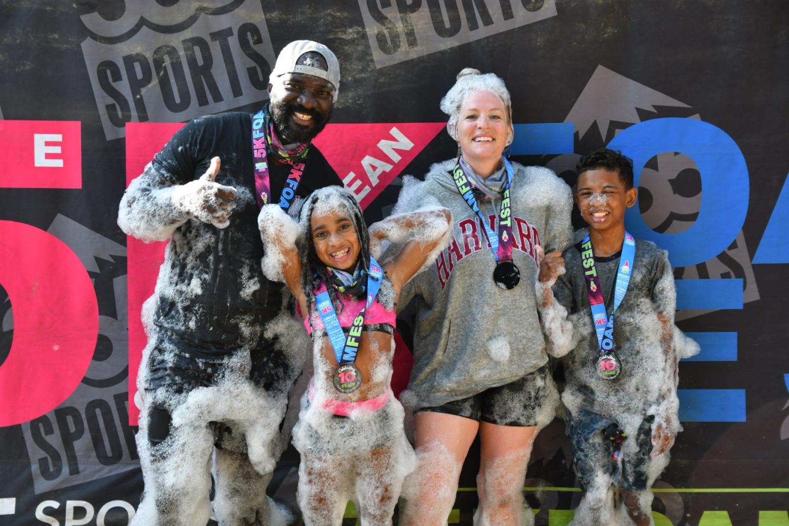 Family smiling in foamy race, wearing medals.