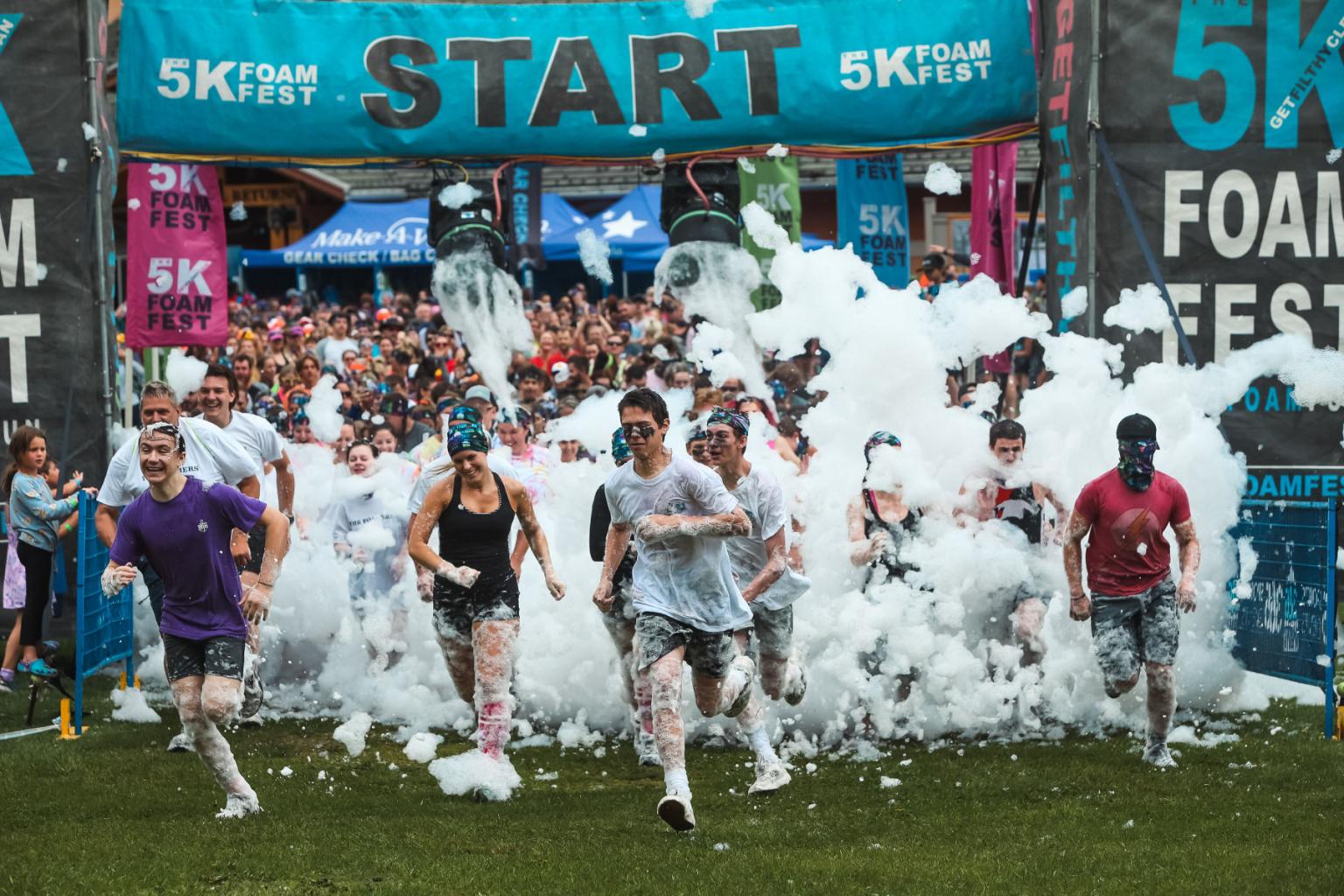 Runners covered in foam start a race, surrounded by cheering crowds.