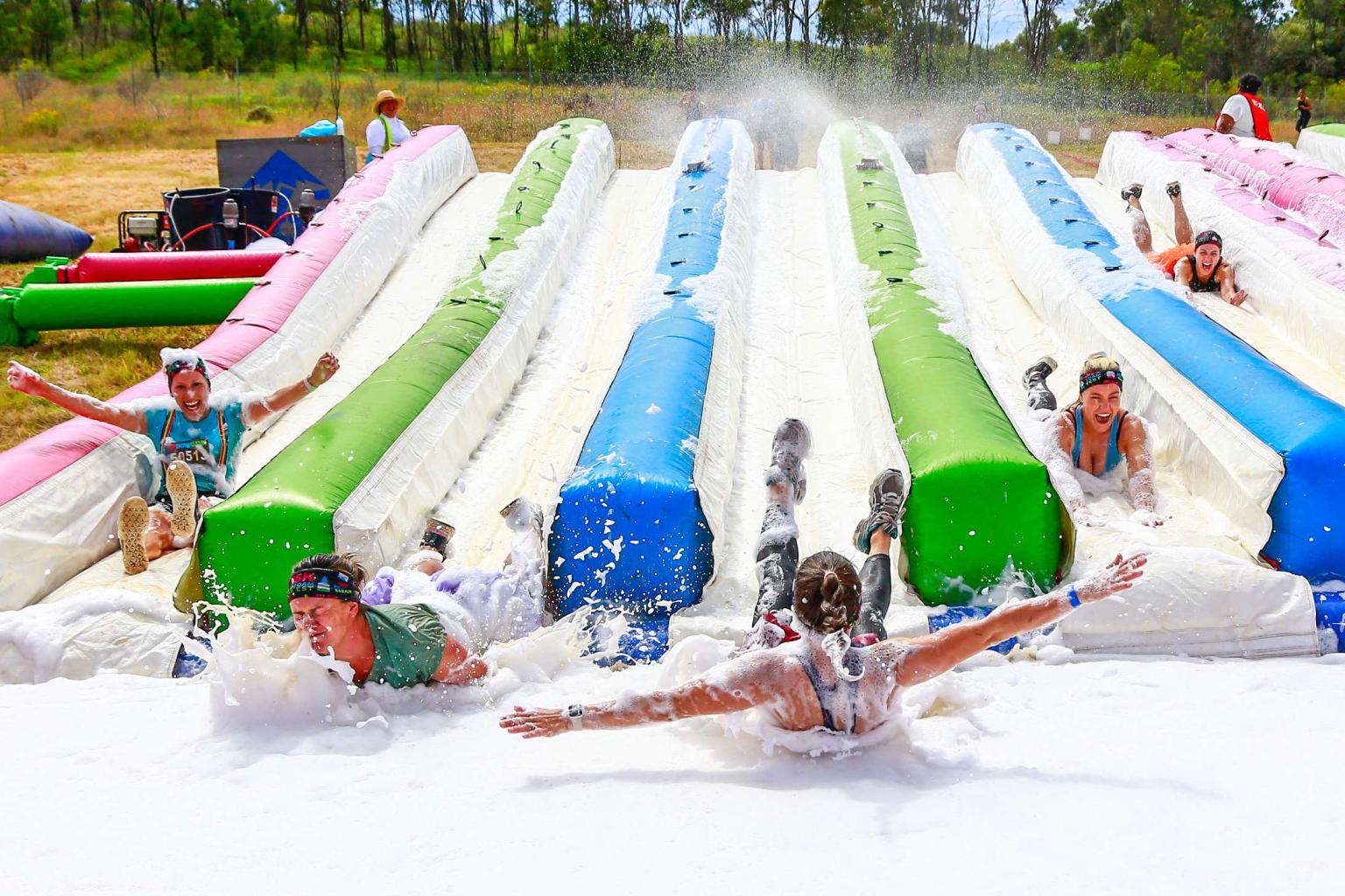 People sliding down colorful inflatable water slides, splashing and laughing.