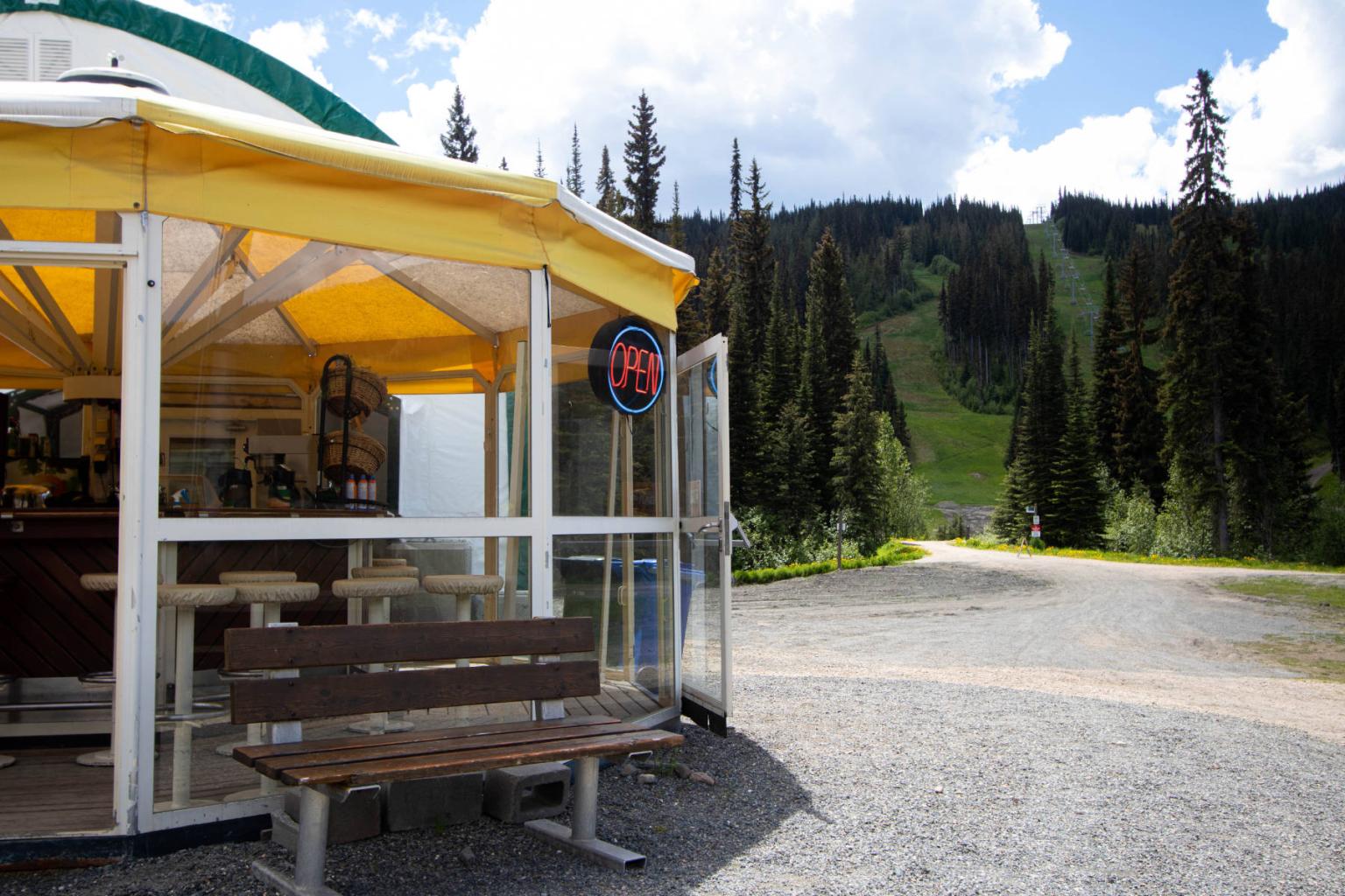 Cafe with yellow awning by a forest trail on a sunny day.