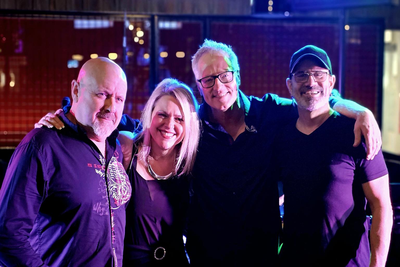Four people standing together, smiling in a dimly lit area.