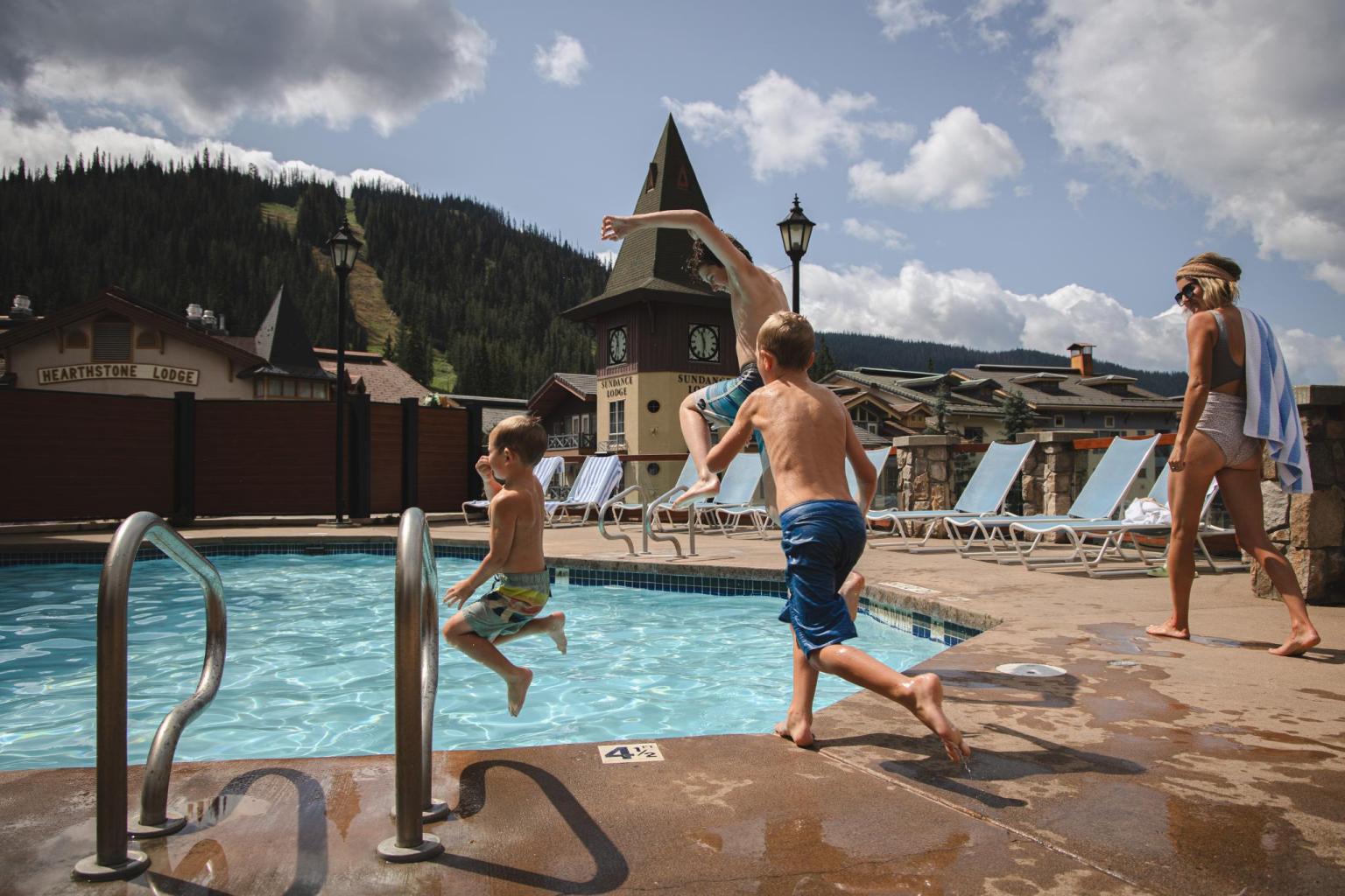 Children jumping into a pool, with mountains and blue sky in the background.