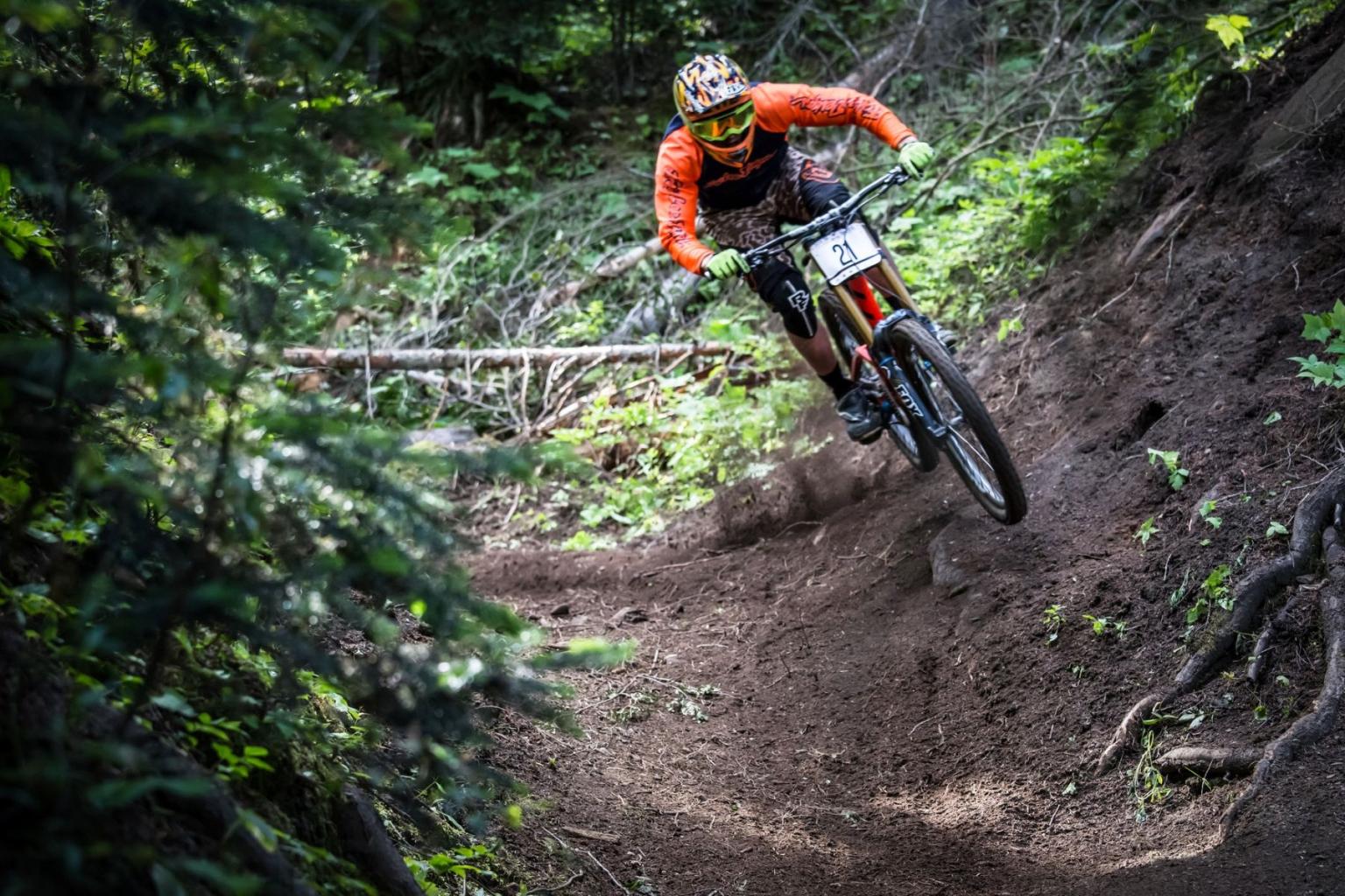 Mountain biker in orange descends a forest trail.