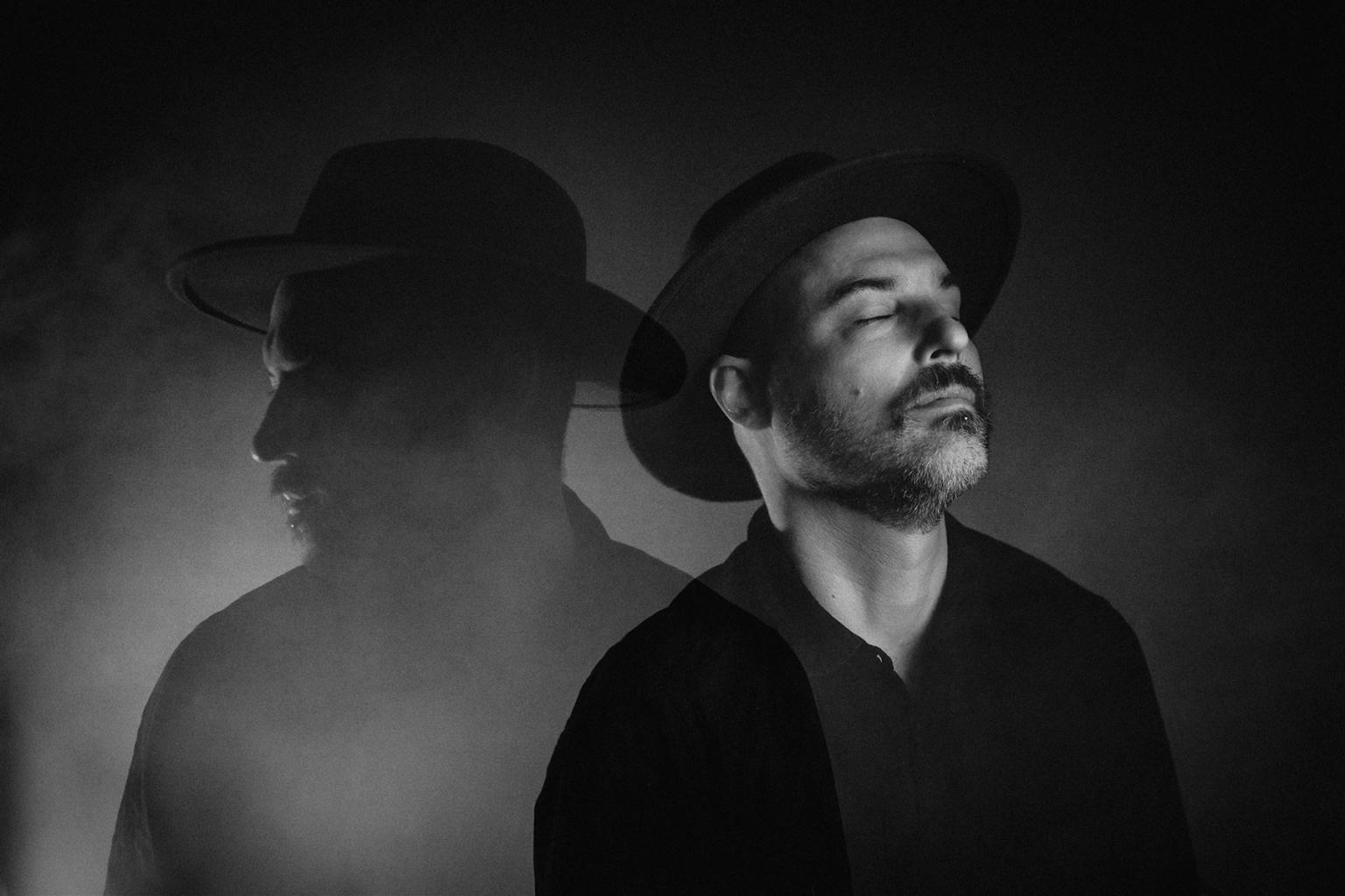 Man in a hat with eyes closed, shadow cast on smoky background, black and white photo.