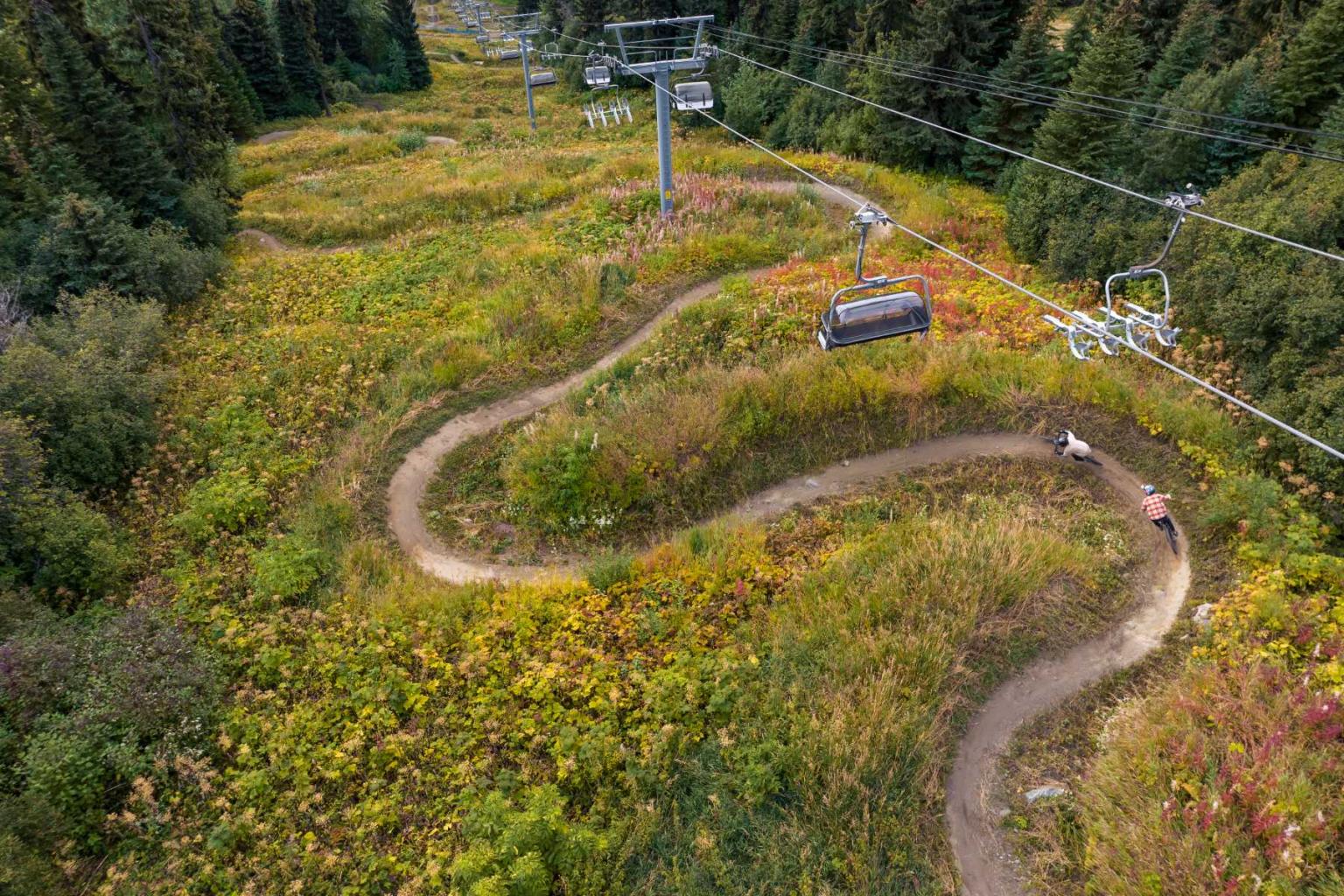 Winding forest trail with a mountain biker and ski lift above.