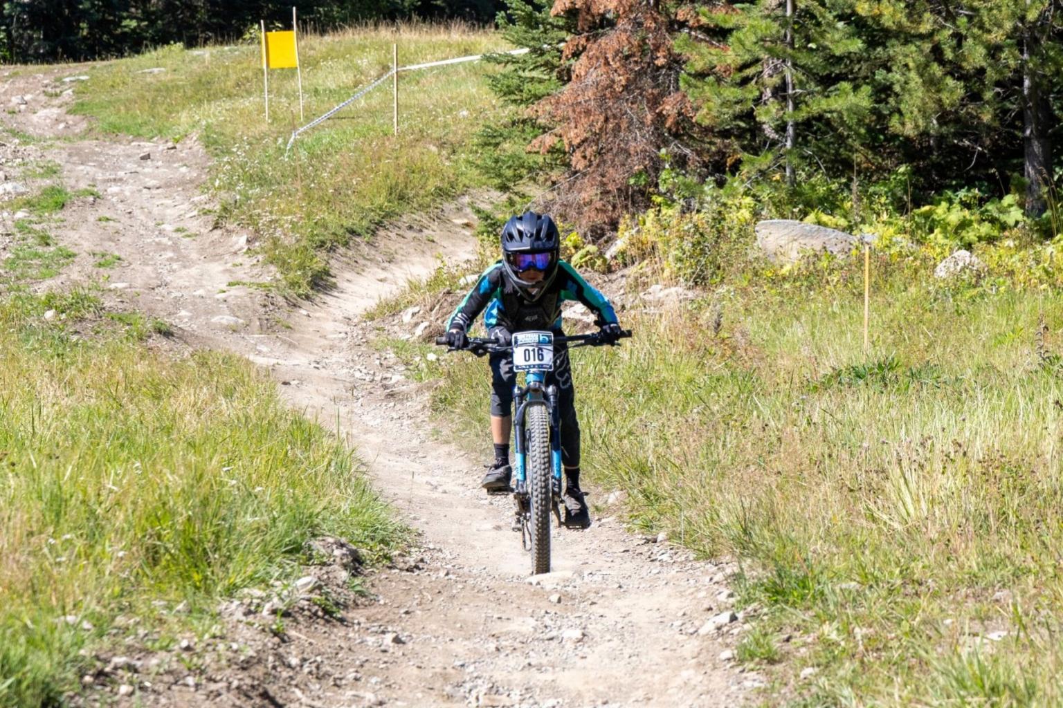 Young mountain biker on a rocky trail surrounded by grass and trees.