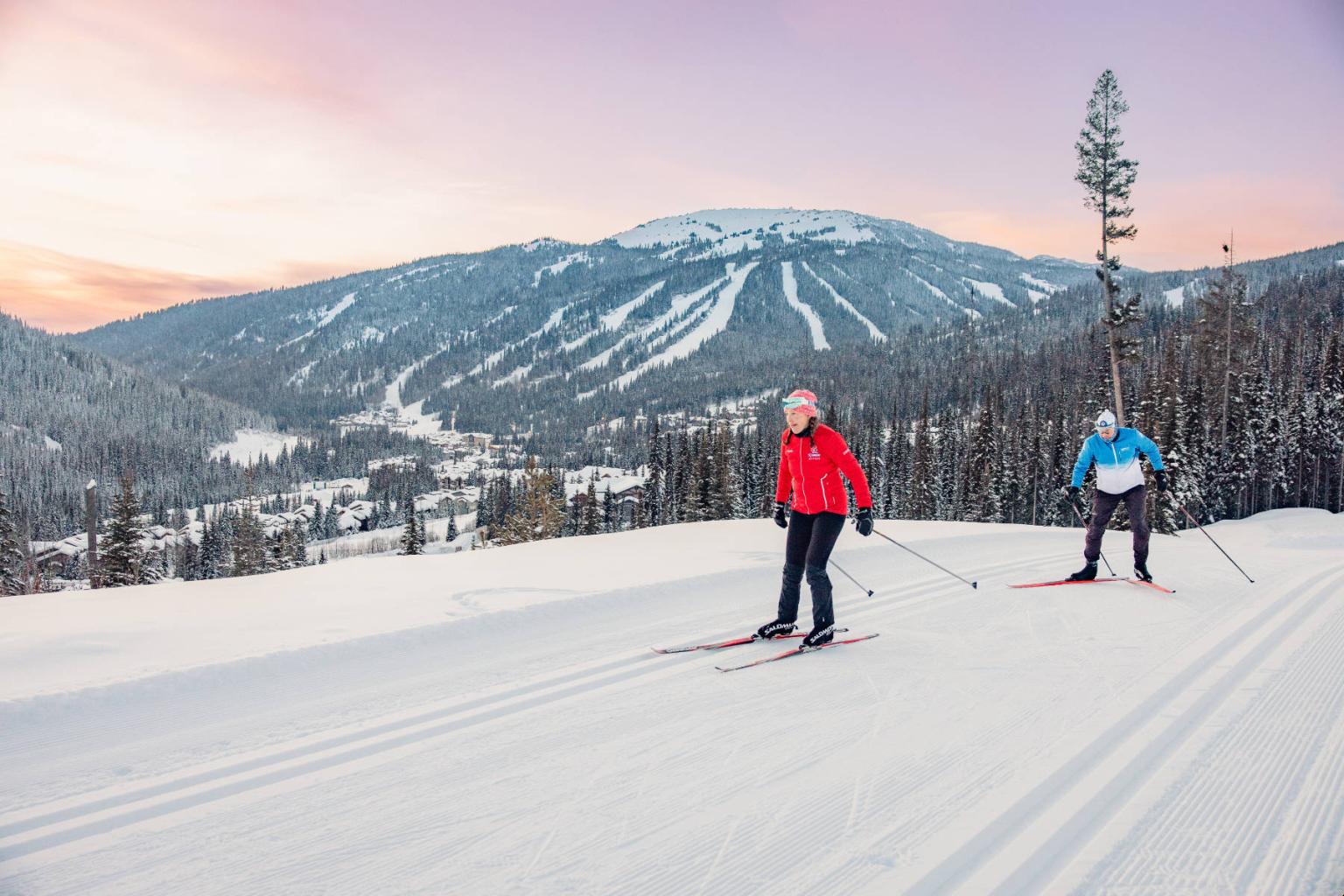 Two people skiing on a snowy mountain at sunset.