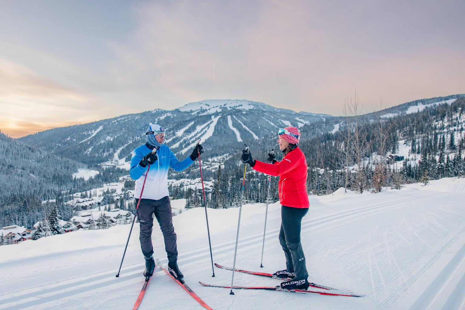 Cross-country skiers on snowy mountain with sunset sky.