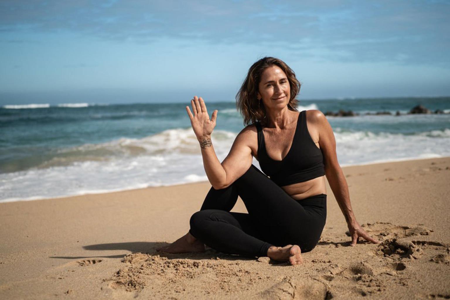 Woman doing yoga on a sandy beach with the ocean in the background.