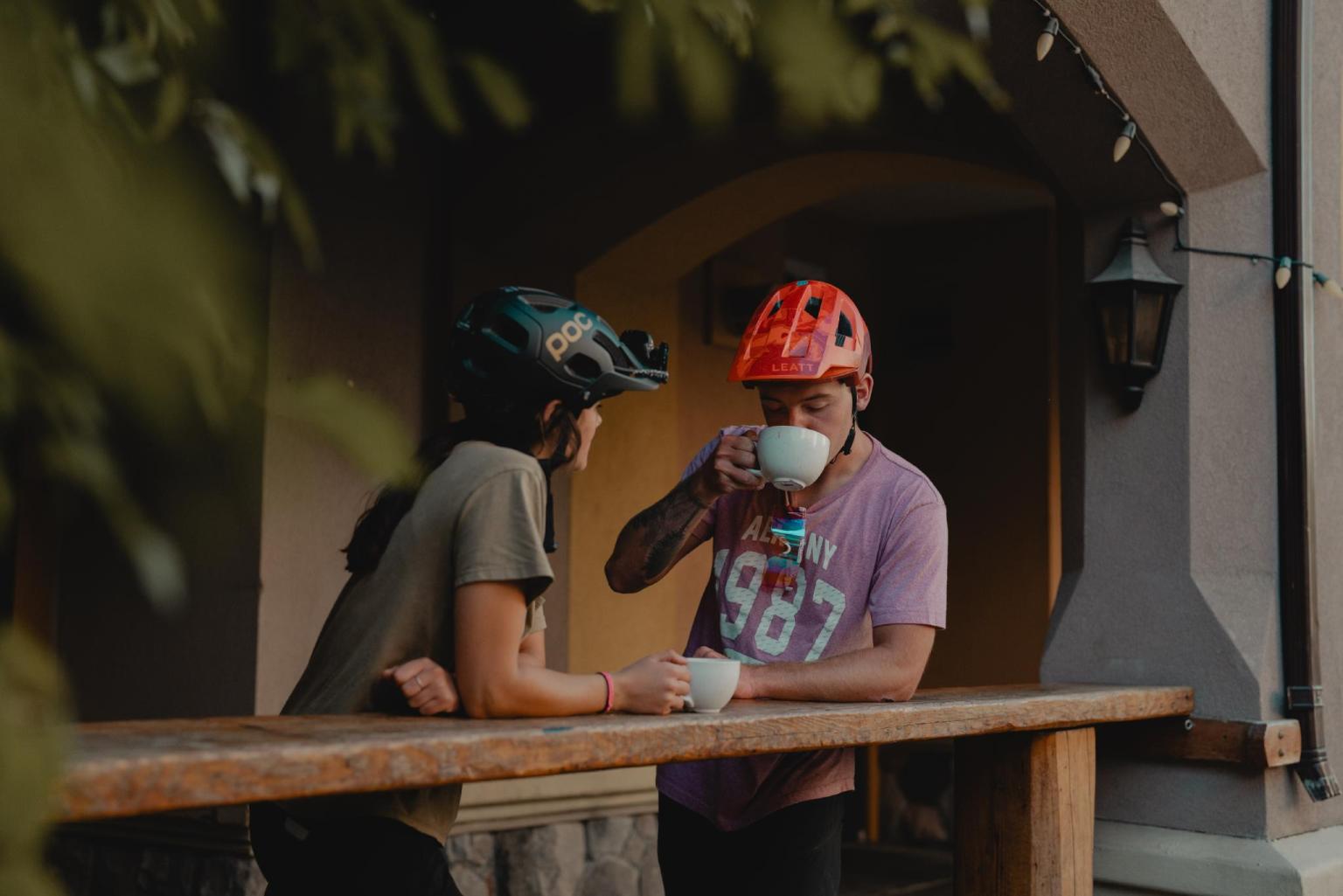 Two people in helmets enjoying coffee on a porch.