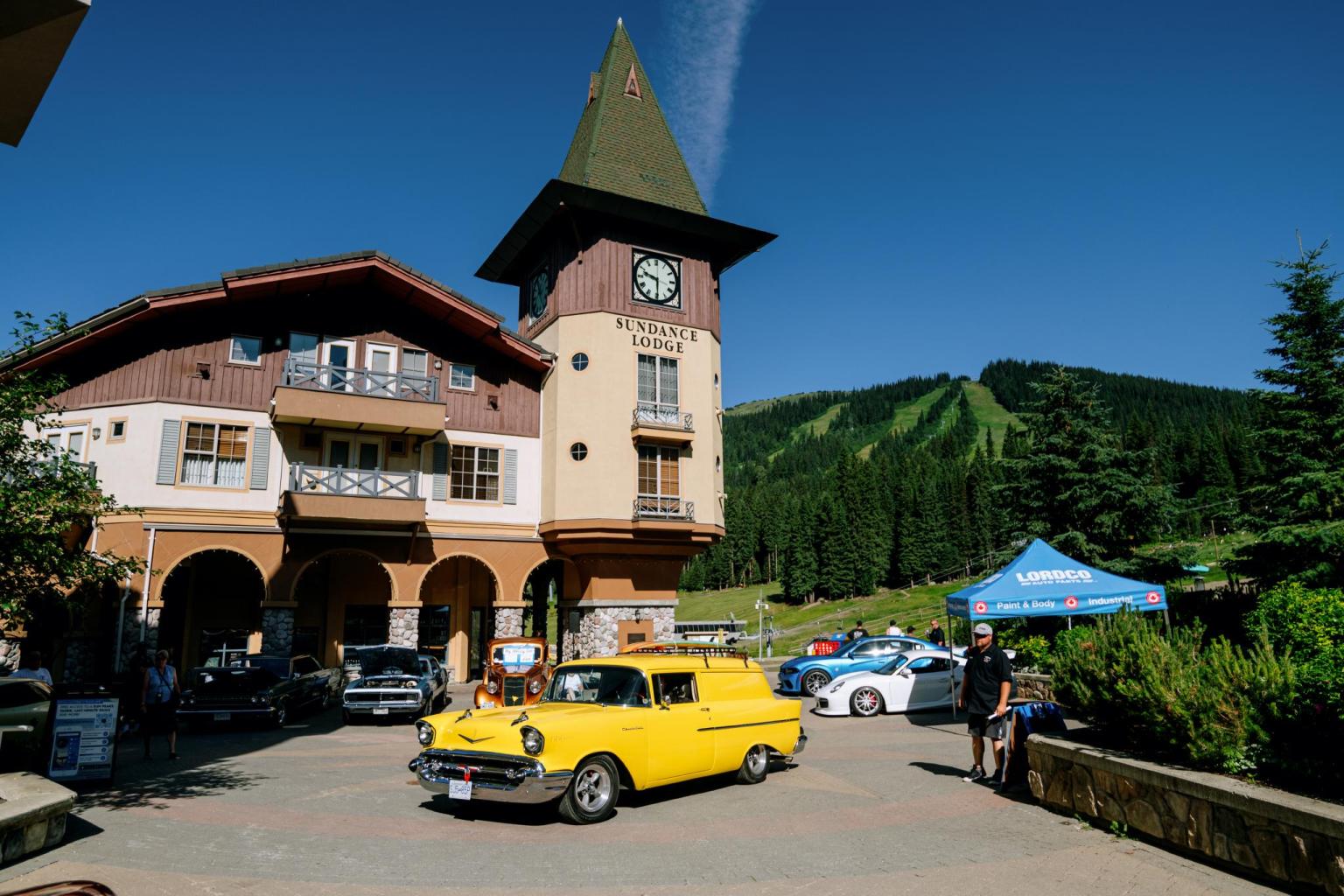 Clock tower building with a yellow vintage car in front, set against a clear blue sky.