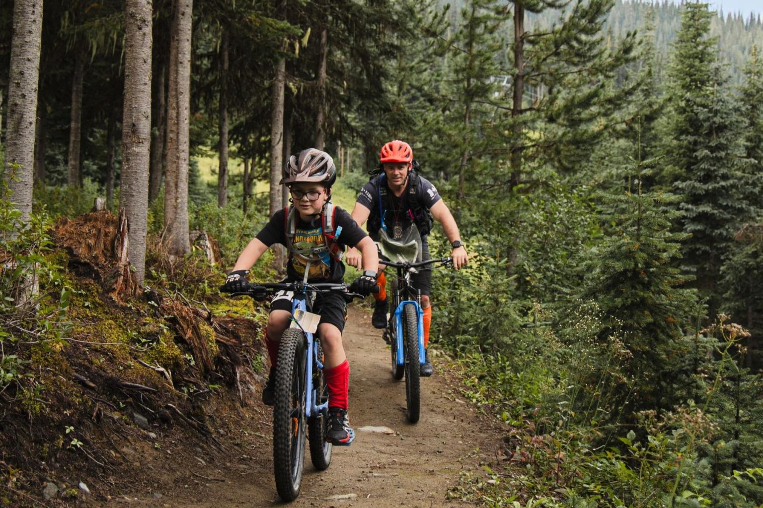 Two mountain bikers riding through a forest trail.