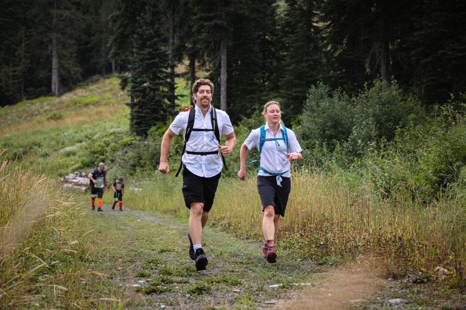 Two people running on a forest trail, smiling.