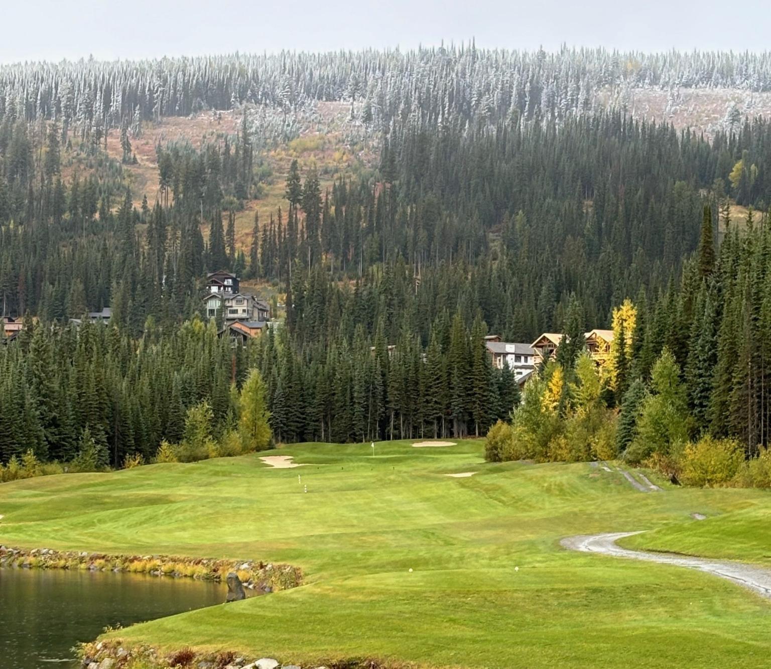 Golf Course with Forest and Mountain with autumn colors, lush green lawn, and a small pond in foreground.