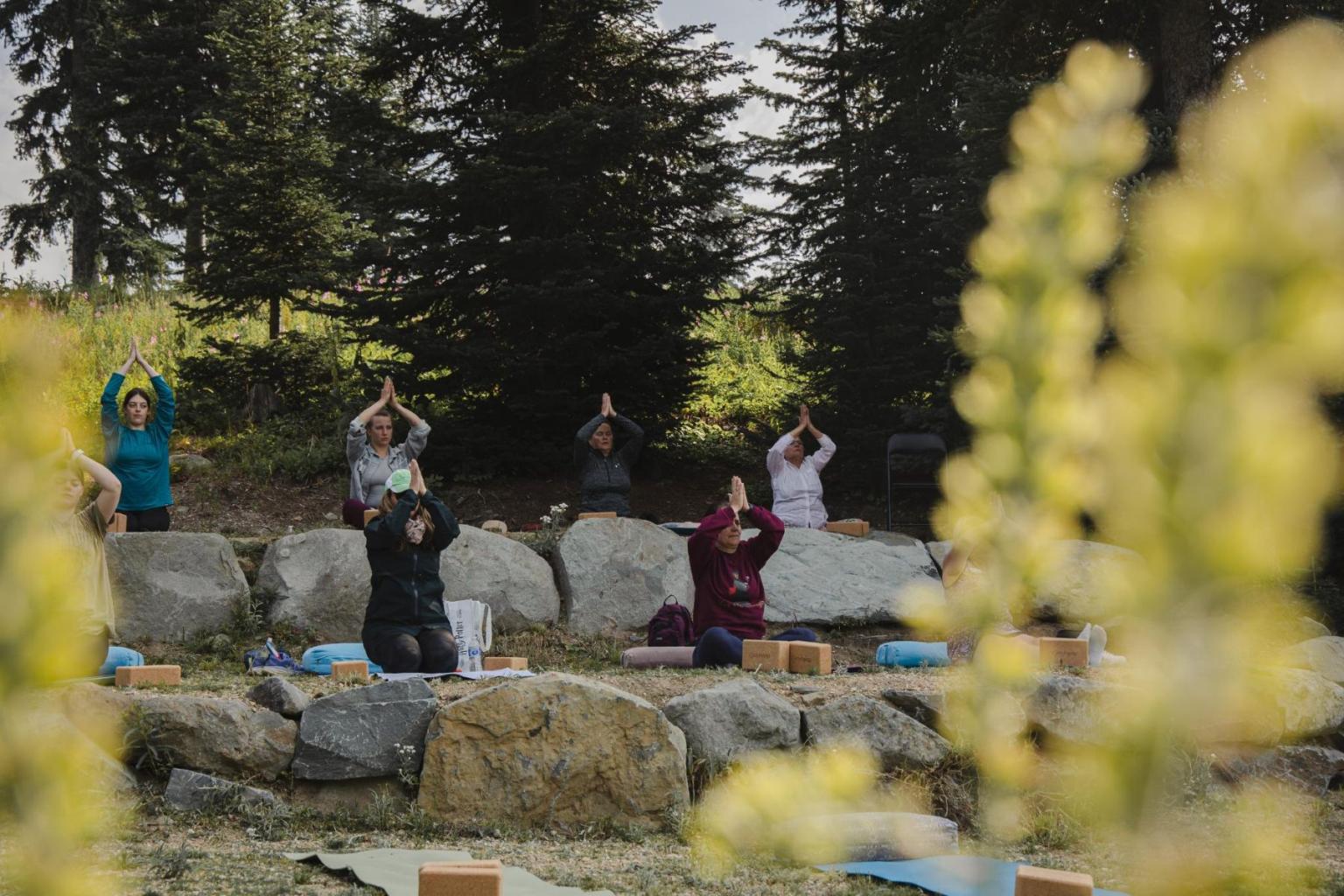 People practicing yoga outdoors, surrounded by trees and rocks in the Sun Peaks wedding area.