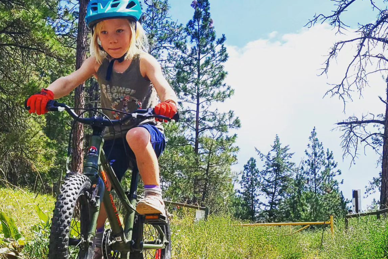 Child biking on a forest trail, wearing a blue helmet and red gloves.