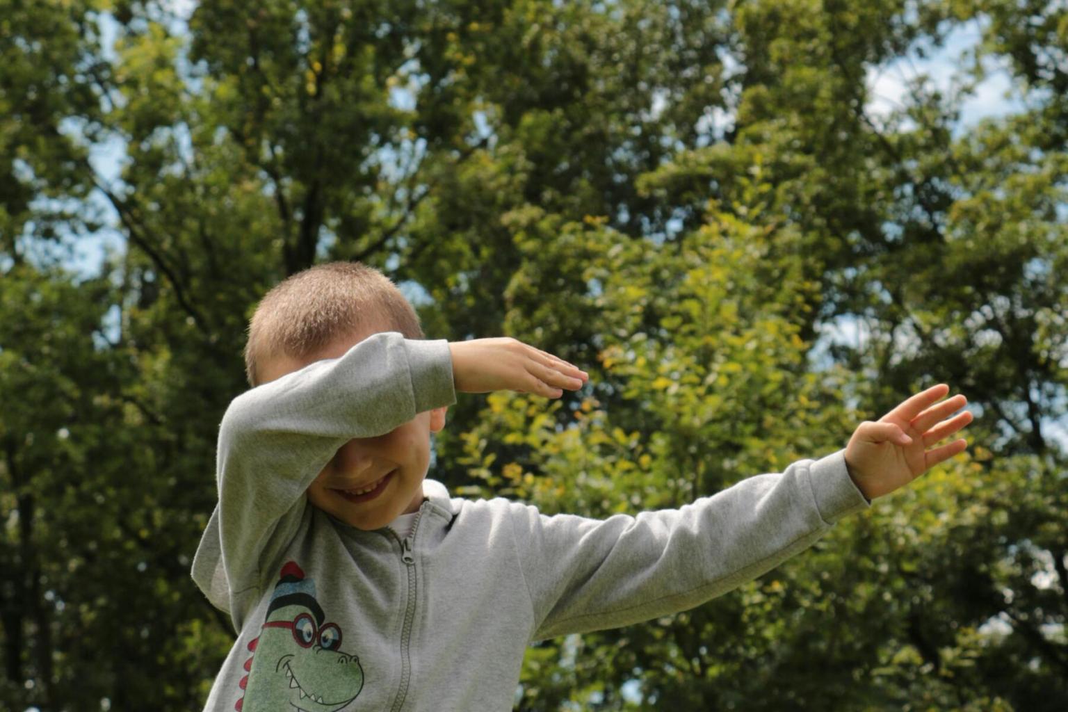 Child doing a dab pose in a sunny park.