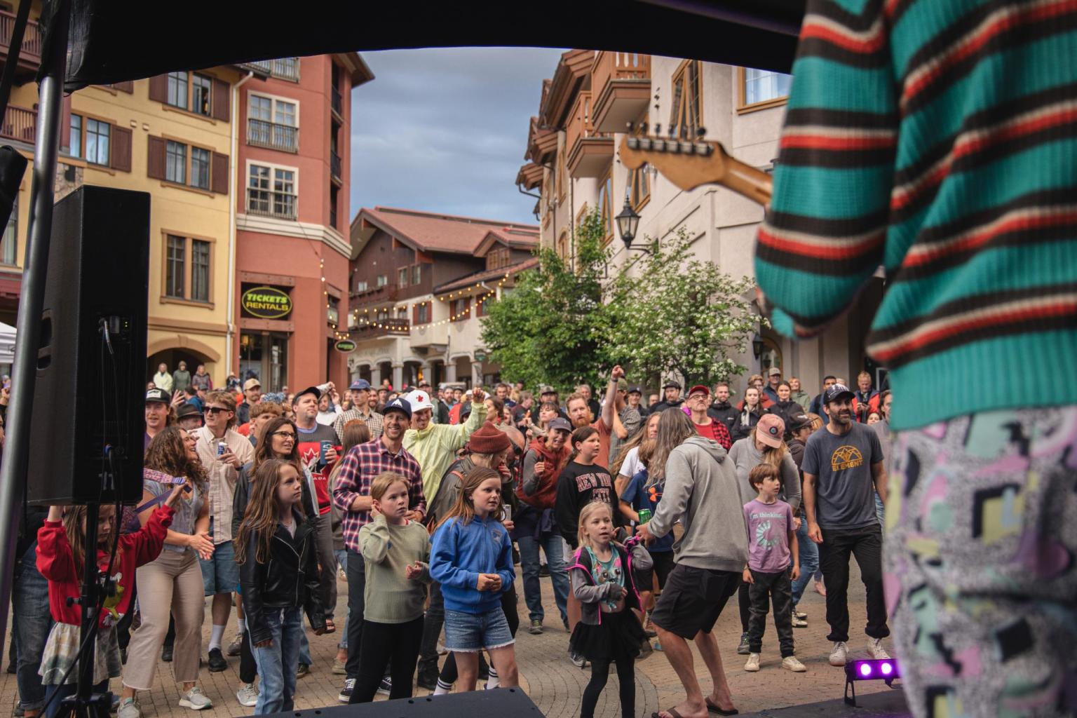 A crowd gathers in a lively outdoor plaza with colorful buildings.