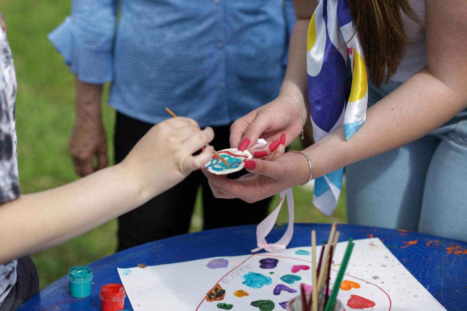 Hand painting a wooden craft with blue paint at an outdoor art table.