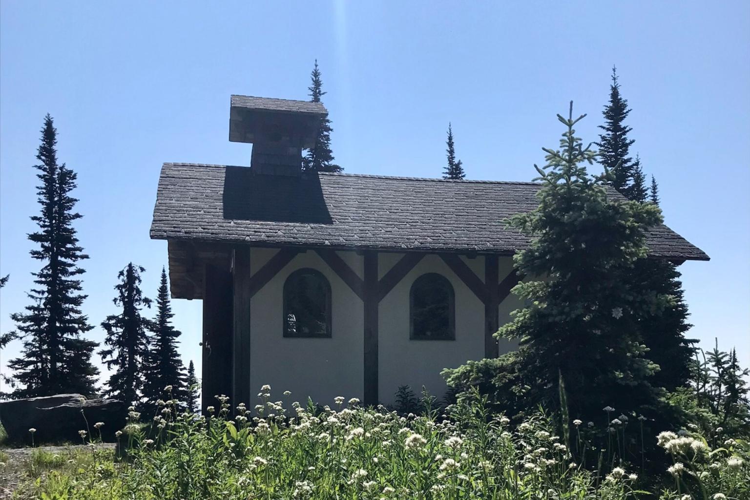 A small chapel surrounded by trees under a clear blue sky.