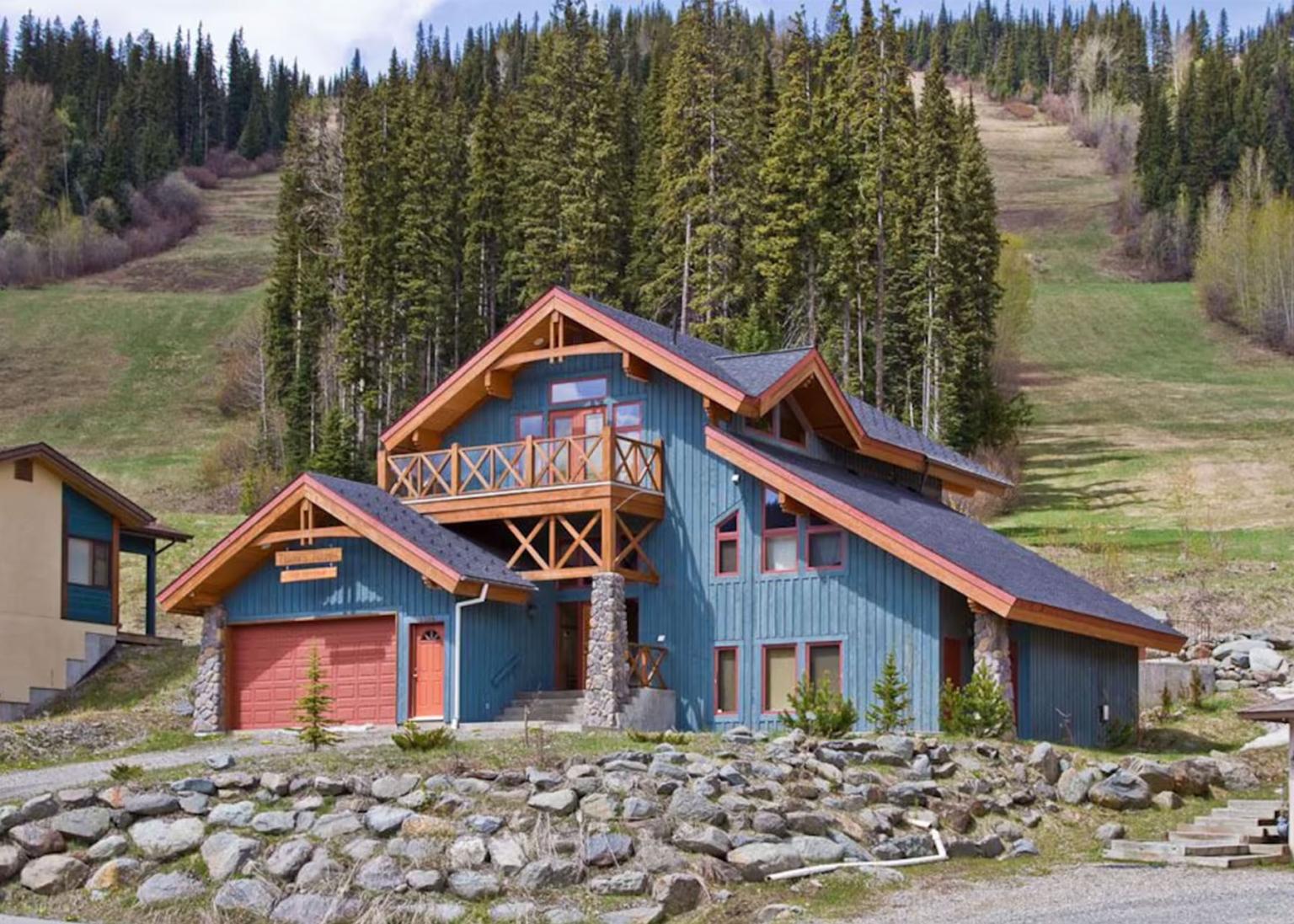 Chalet-style house with wood accents, pine forest backdrop.
