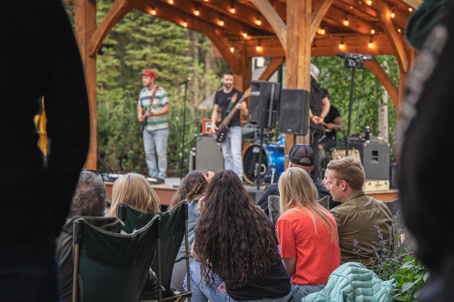 Outdoor concert with a band performing on stage; audience seated in the foreground.