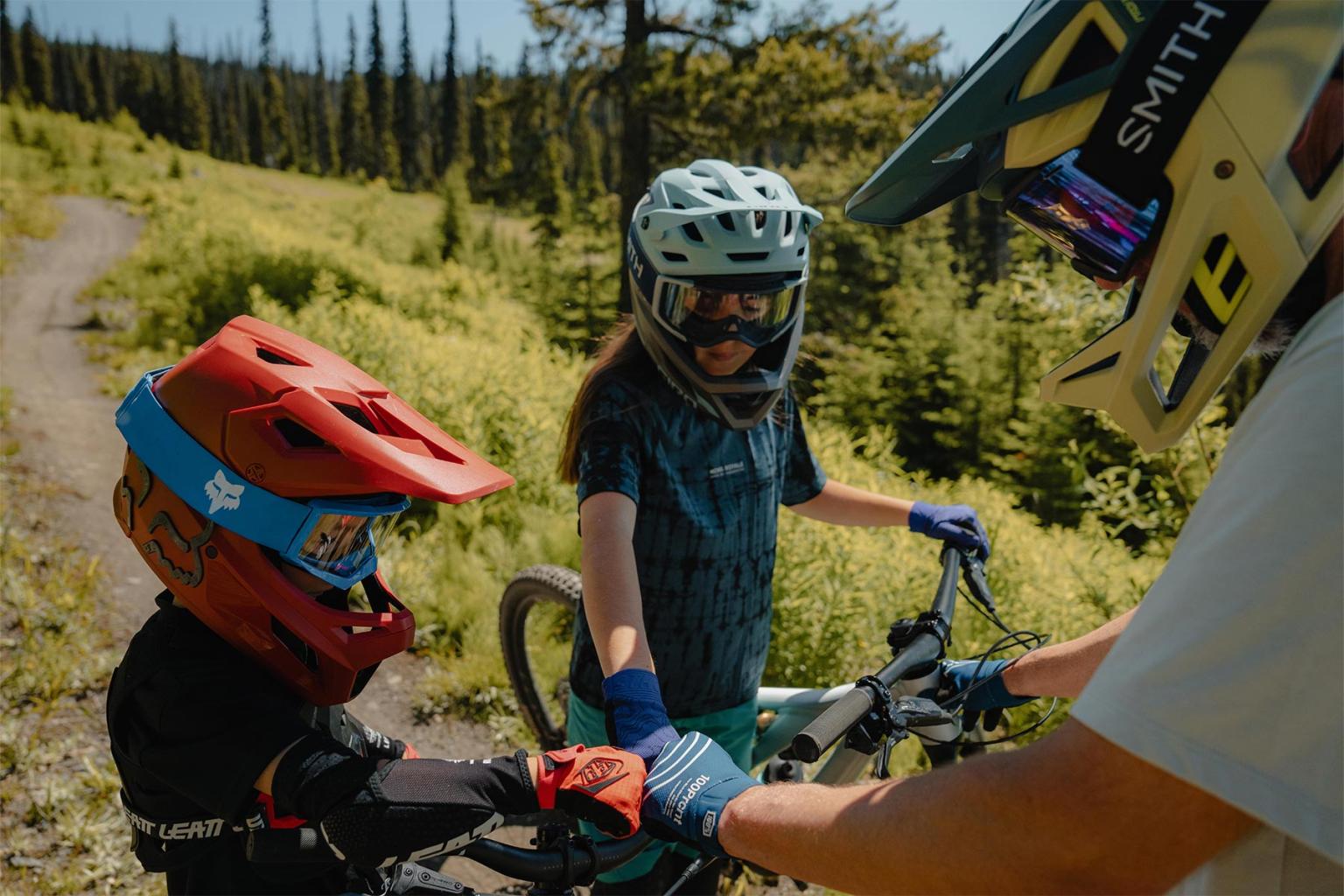 Bikers with helmets on a sunny forest trail, holding handlebars together.