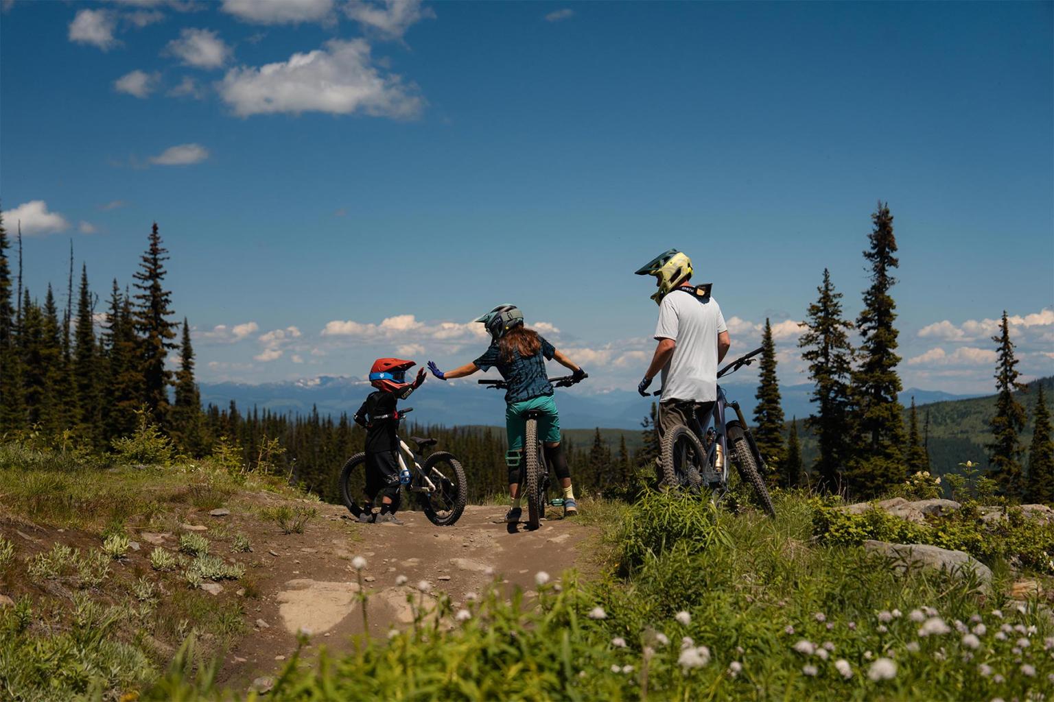Mountain bikers high-five on a trail with scenic views.