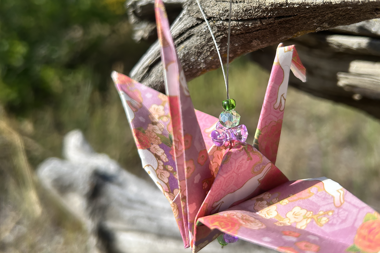Origami crane with floral patterns, hanging on string outdoors.
