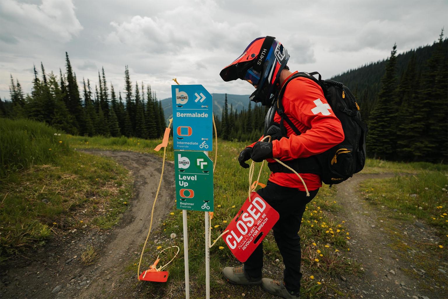 Patroller putting up trail signs with trees behind him. 