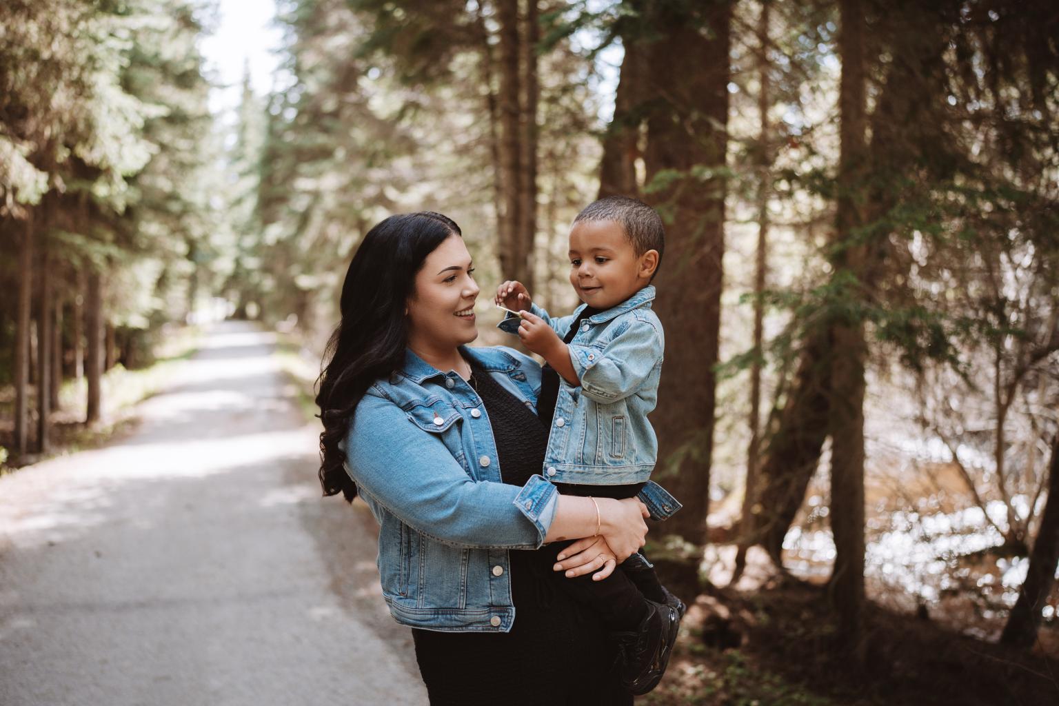 Mother and child in denim jackets on a forest path, smiling.