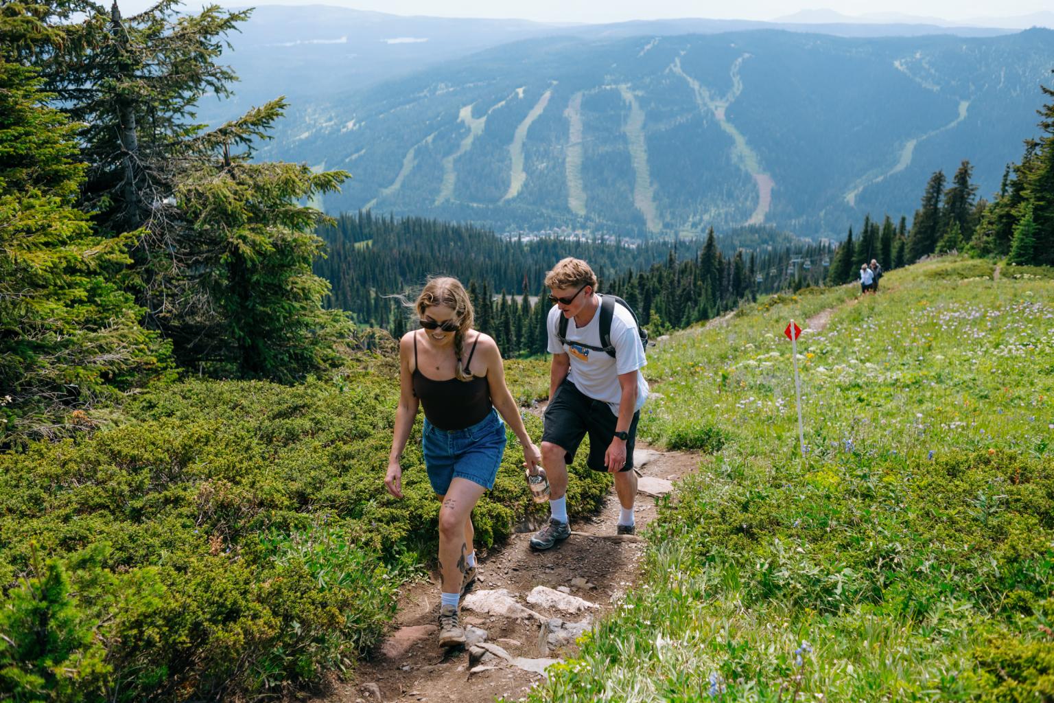 Two people hiking on a mountain trail with a scenic view in the background.