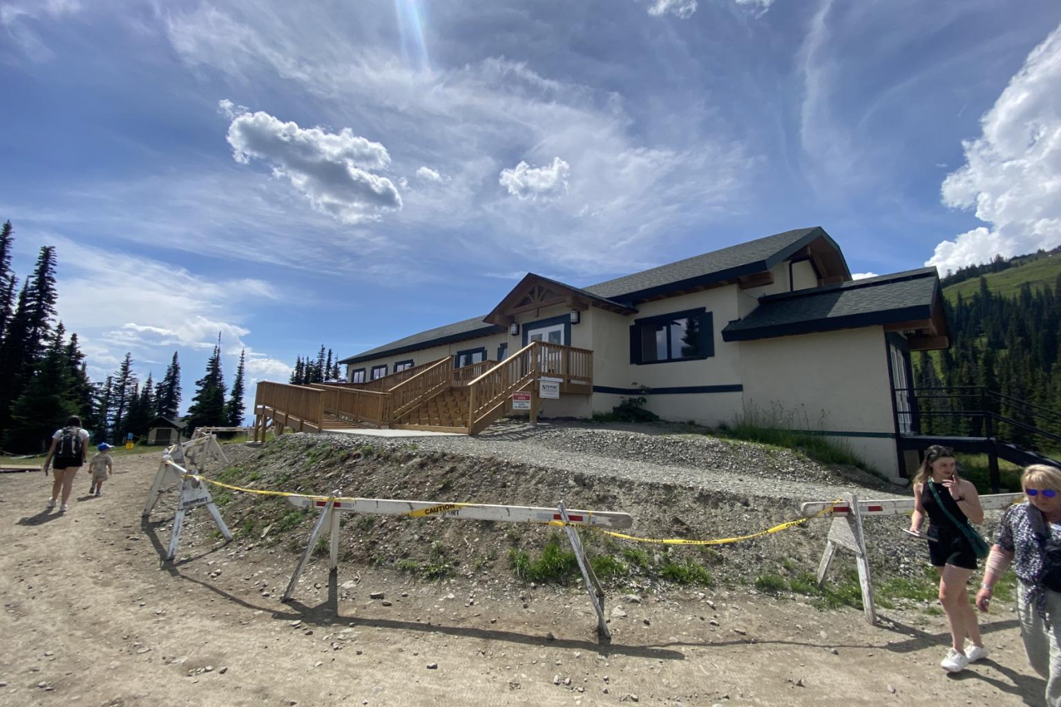 Sunburst mid-mountain lodge under a cloudy blue sky with surrounding trees and hikers.