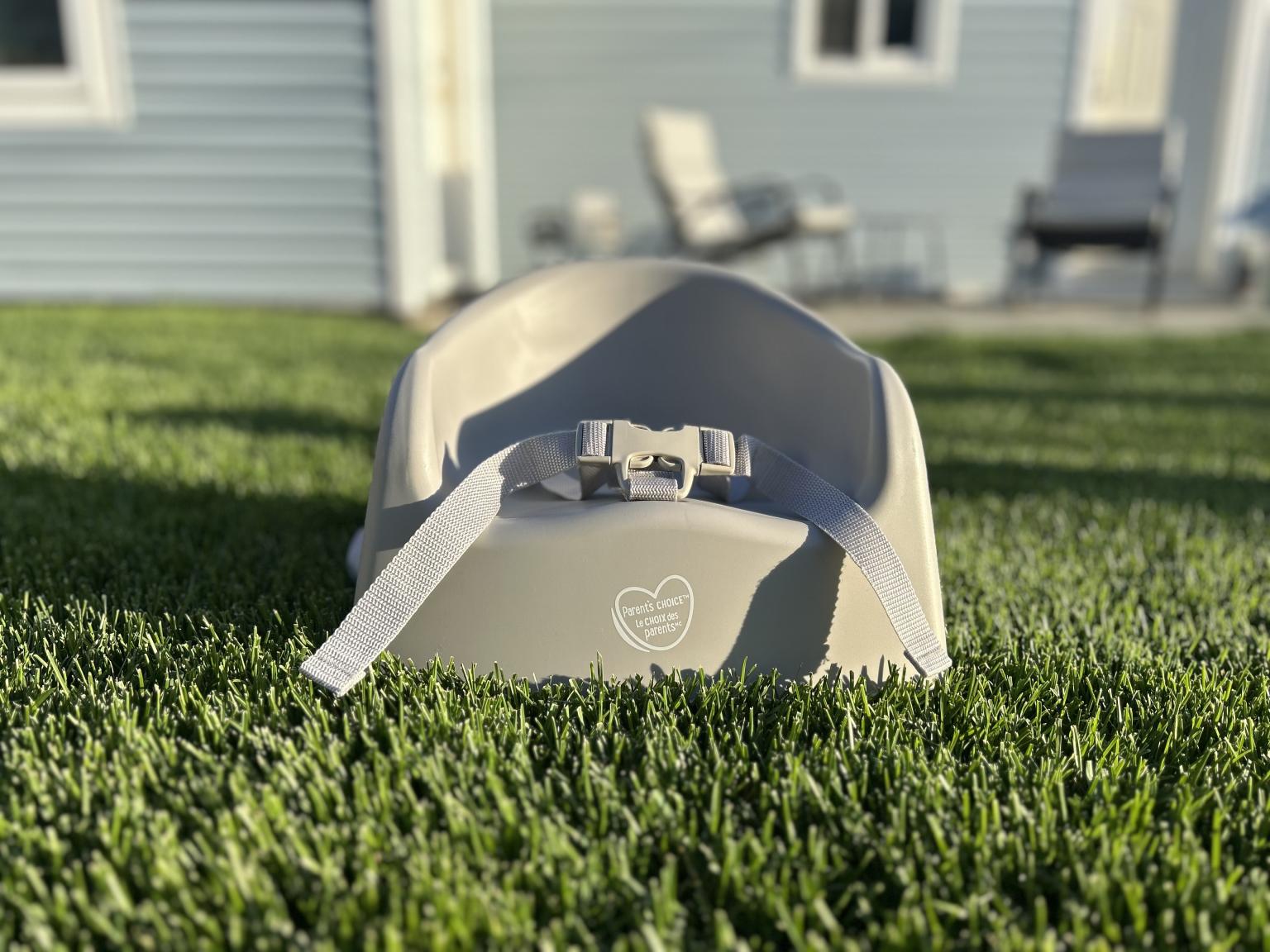 Gray baby seat on grass, house and chairs in the background.