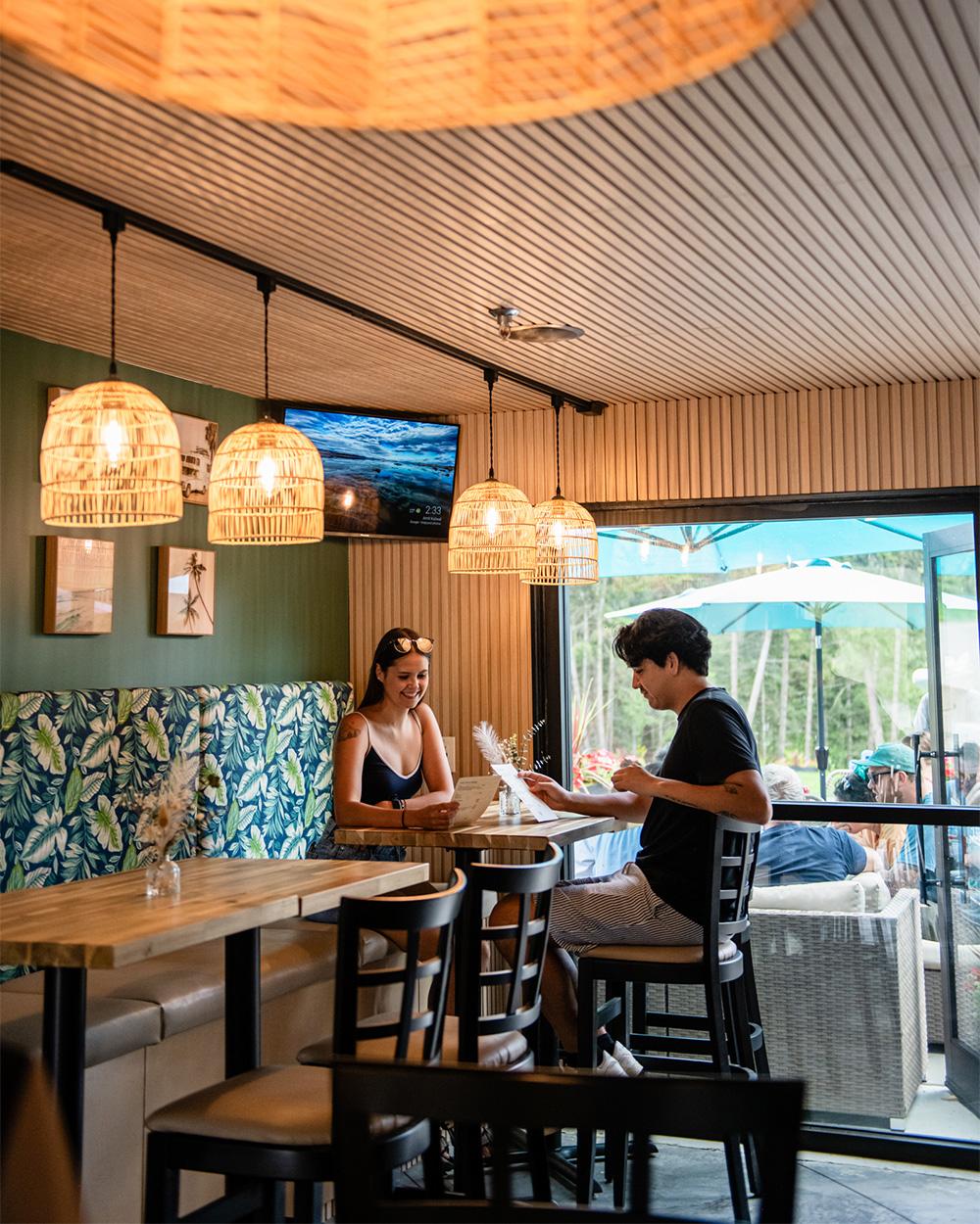 Cozy bistro with two people sitting, hanging lights, and an outdoor view.