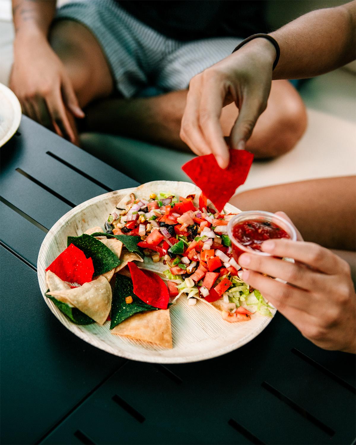 Plate of nachos with salsa and colorful chips on a dark table.