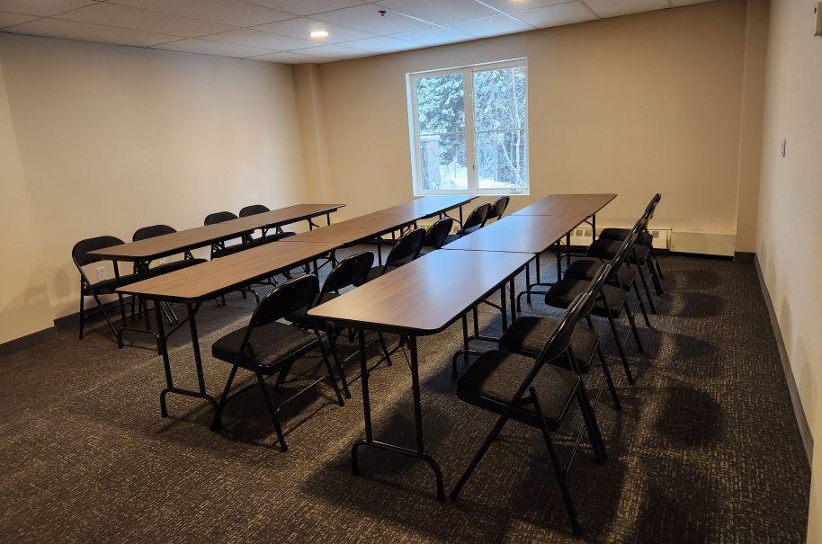 Empty meeting room with tables, chairs, and a window.