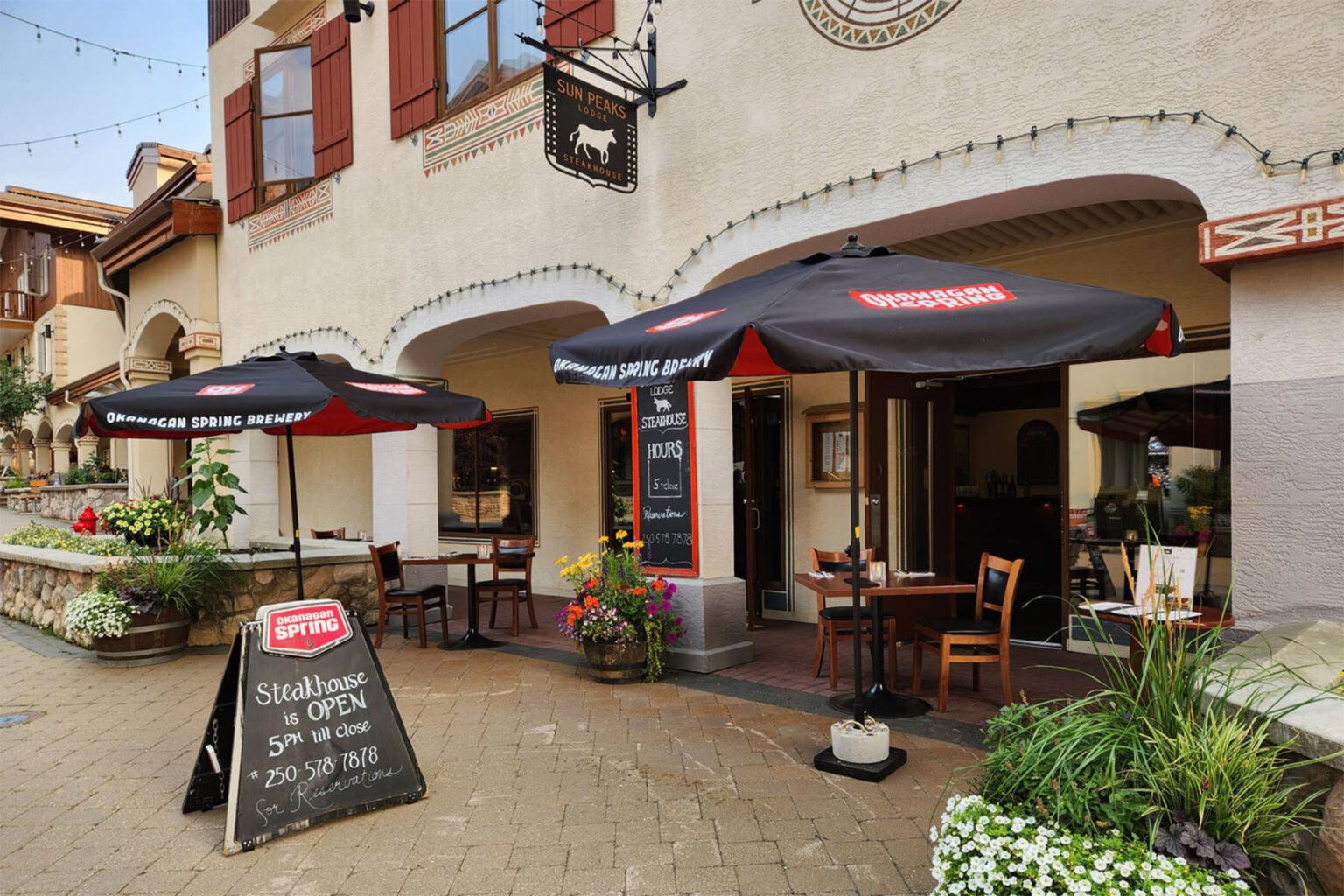 Outdoor cafe with black umbrellas, chairs, and tables on a cobblestone patio.