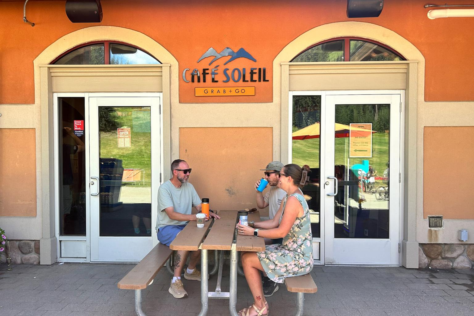 Outdoor cafe with three people seated at a table, warm sunny setting.