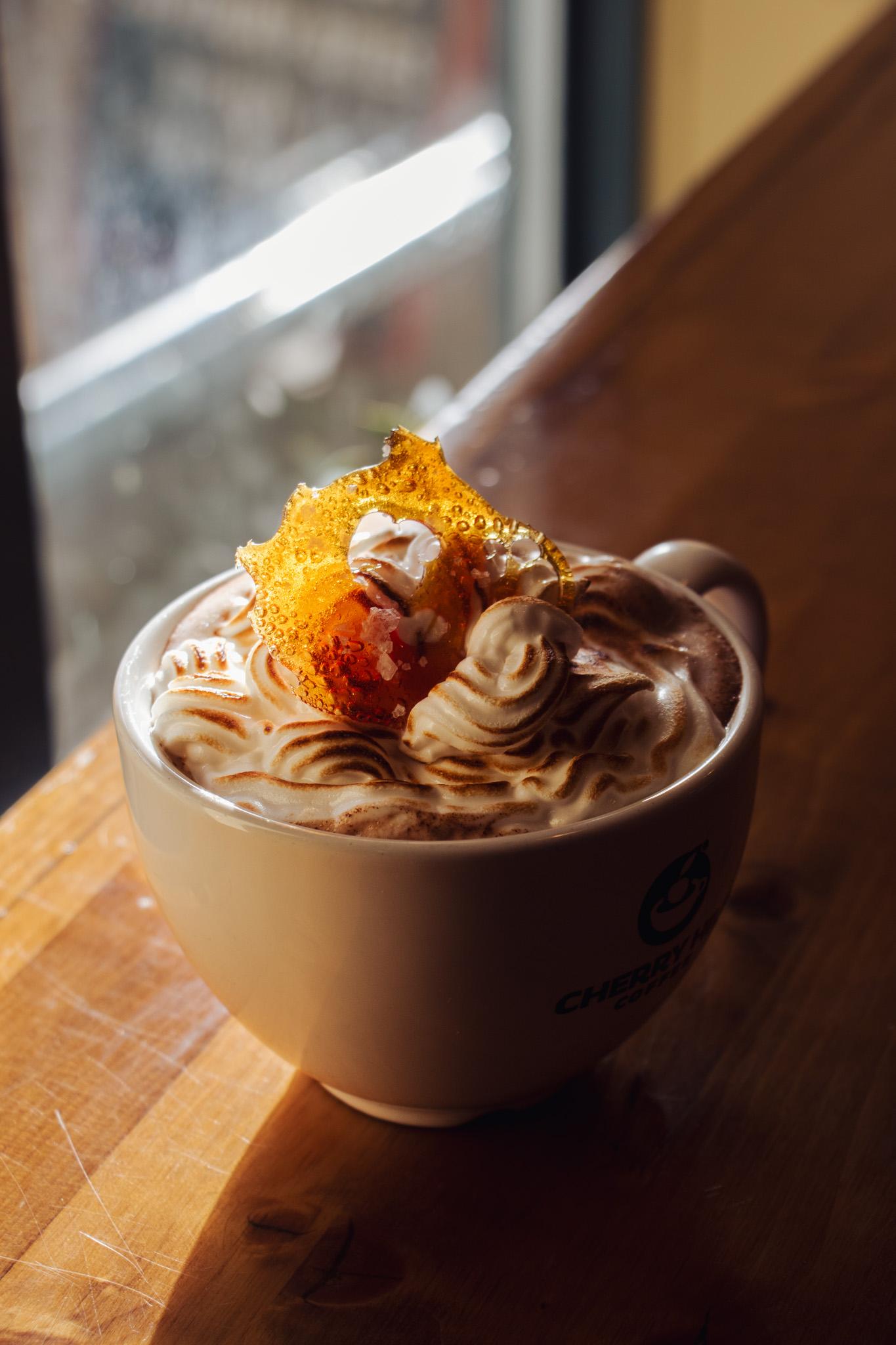 A cup of whipped cream-topped coffee with caramel drizzle on a wooden table.