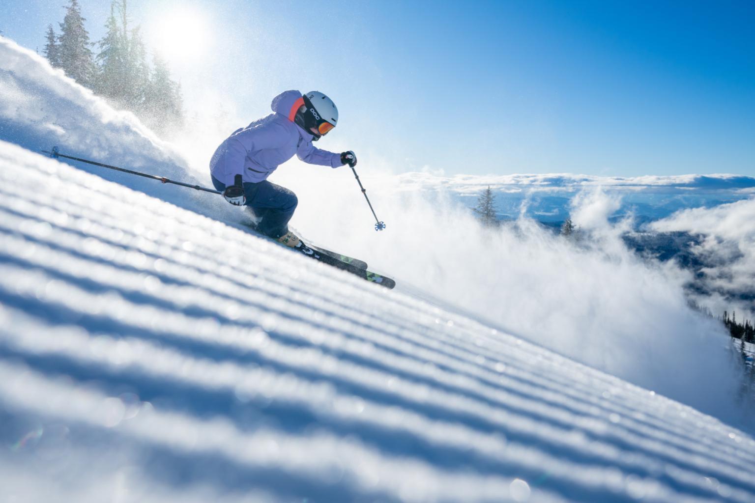 Skier in purple jacket descends a snowy slope under a clear blue sky.
